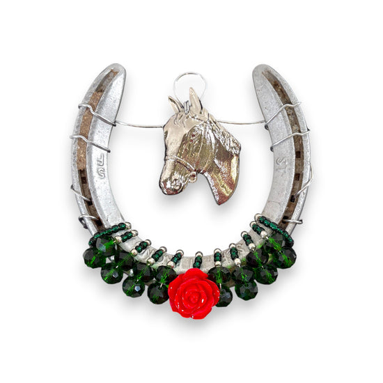 The authentic metal horseshoe adorned with a silver horsehead charm and a single rose, hanging on a wall.
