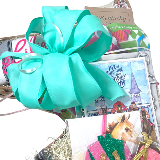 Gift basket with a large turquoise bow, Kentucky Derby-themed items, and a horse race poster.