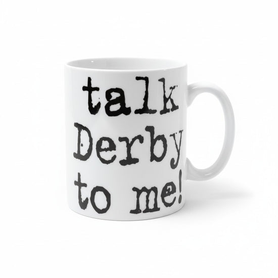 A white ceramic coffee mug featuring the playful text Talk Derby to Me printed on the front