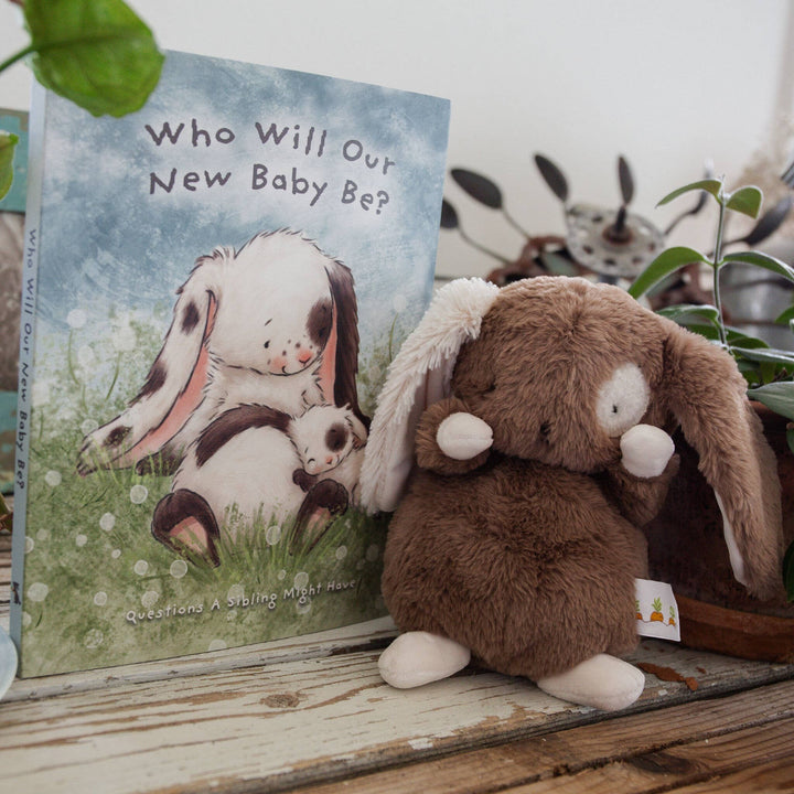 A Taste of Kentucky "Who Will Our New Baby Be?" hardcover story book for ages 0-3, featuring illustrated bunnies. A brown plush bunny sits beside it.
