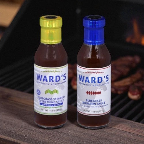 Two bottles of Ward's Bluegrass Sauces on a grill with skewers in the background.