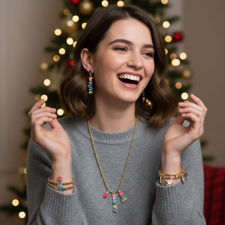A woman laughing while wearing the Merry & Bright jewelry in front of a festive Christmas tree.