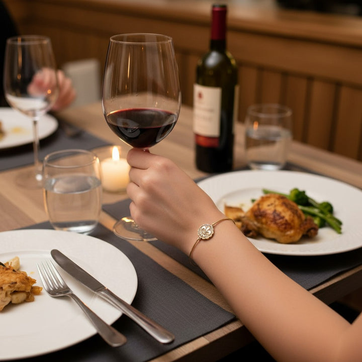 A lifestyle photo showing a woman wearing the fleur de lis coin bangle while holding a glass of wine.