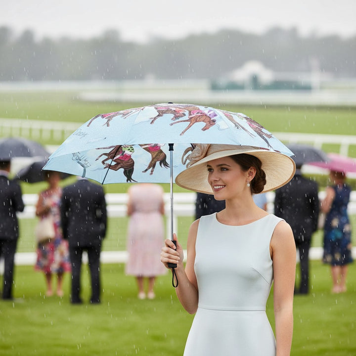 A woman in a stylish race day hat and dress smiles while holding the open Art of the Derby 152 umbrella during a light rain at a racetrack.