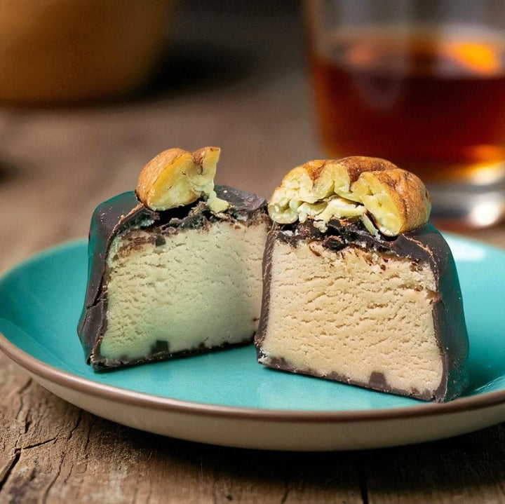 Two pieces of ice cream cake on a turquoise plate with a glass of amber liquid in the background.