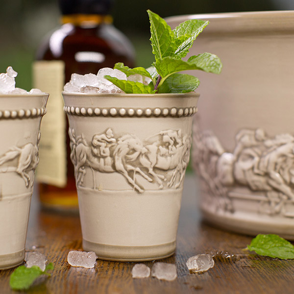 Tan Mint Julep Cup with embossed Racing Horses filled with ice and mint sprig, on wooden table. Stoneware & Co, Louisville Stoneware