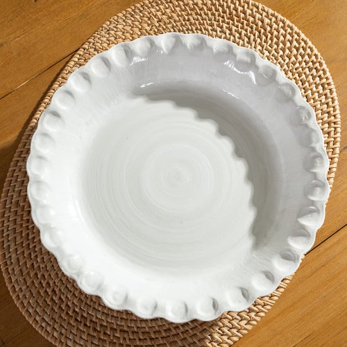 Tan pie plate with white interior sitting on a wooden table with a beige placemat