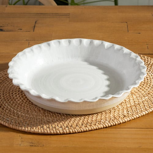 Tan pie plate with white interior sitting on a wooden table with a beige placemat